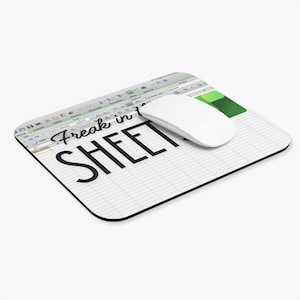 May include: A rectangular mouse mat featuring a spreadsheet design with the text "Freak in SHEET" in black. A white wireless mouse sits on the mat. The mat has a black border and a green accent.