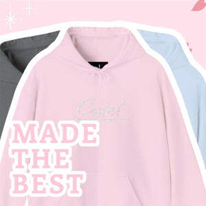 May include: Three hoodies in gray, pink, and light blue. The pink hoodie has the word "Cute!" in silver glitter and the words "MADE THE BEST" in pink block letters. The hoodies have drawstrings and a hood.