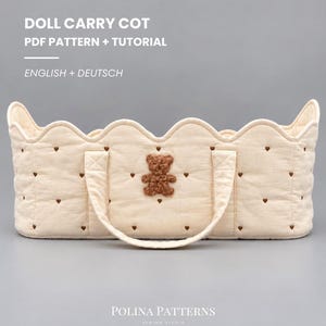 Peut inclure: Un couffin pour poupée matelassé de couleur crème avec un bord supérieur festonné, deux poignées en tissu et une application d'ours en peluche marron. L'extérieur est orné de petits cœurs brodés marron. Texte : DOLL CARRY COT PDF PATTERN + TUTORIAL ENGLISH + DEUTSCH POLINA PATTERNS.