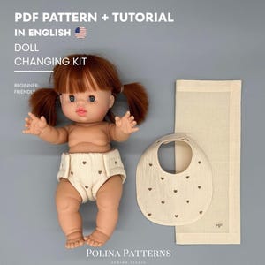 Könnte beinhalten: Eine Puppe mit roten Zöpfen, die eine Windel trägt. Ein Lätzchen und eine Wickelunterlage befinden sich neben der Puppe. Das Lätzchen und die Windel haben ein Herzmuster. Der Text auf dem Bild lautet "PDF PATTERN + TUTORIAL IN ENGLISH DOLL CHANGING KIT BEGINNER-FRIENDLY".