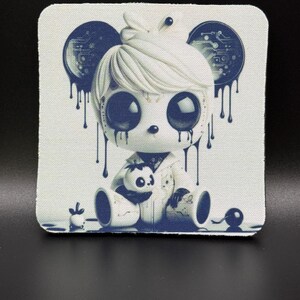 May include: Square white fabric with a cartoon illustration of a doll-like figure with large eyes and dark blue accents. The figure has white hair and is holding a small panda. Dark blue drips and circuit board designs are also present.