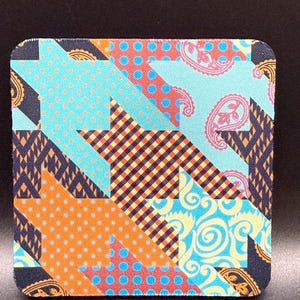 May include: Square coaster with a patchwork design. The coaster features a mix of patterns, including polka dots, paisley, and plaid, in shades of orange, blue, and yellow. The corners are dark blue with a gold paisley design.