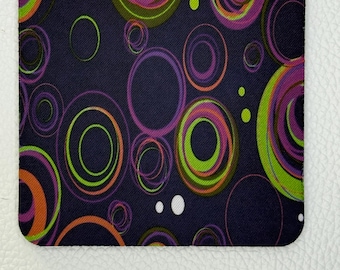 May include: A rectangular mousepad with a dark blue background and a pattern of overlapping circles in shades of green, orange, and purple. The mousepad has rounded corners and a textured surface.