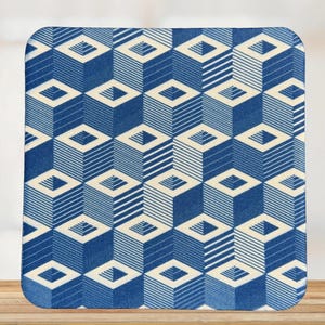 May include: Square coaster with a geometric pattern of blue and off-white cubes and diamond shapes. The design features alternating striped and solid cube faces, creating a 3D effect. The coaster is placed on a wooden surface.