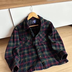 May include: A plaid flannel shirt in a classic pattern of navy, green, red, and yellow. The shirt has two chest pockets, a button-down front, and long sleeves. The shirt is hanging on a wooden hanger.