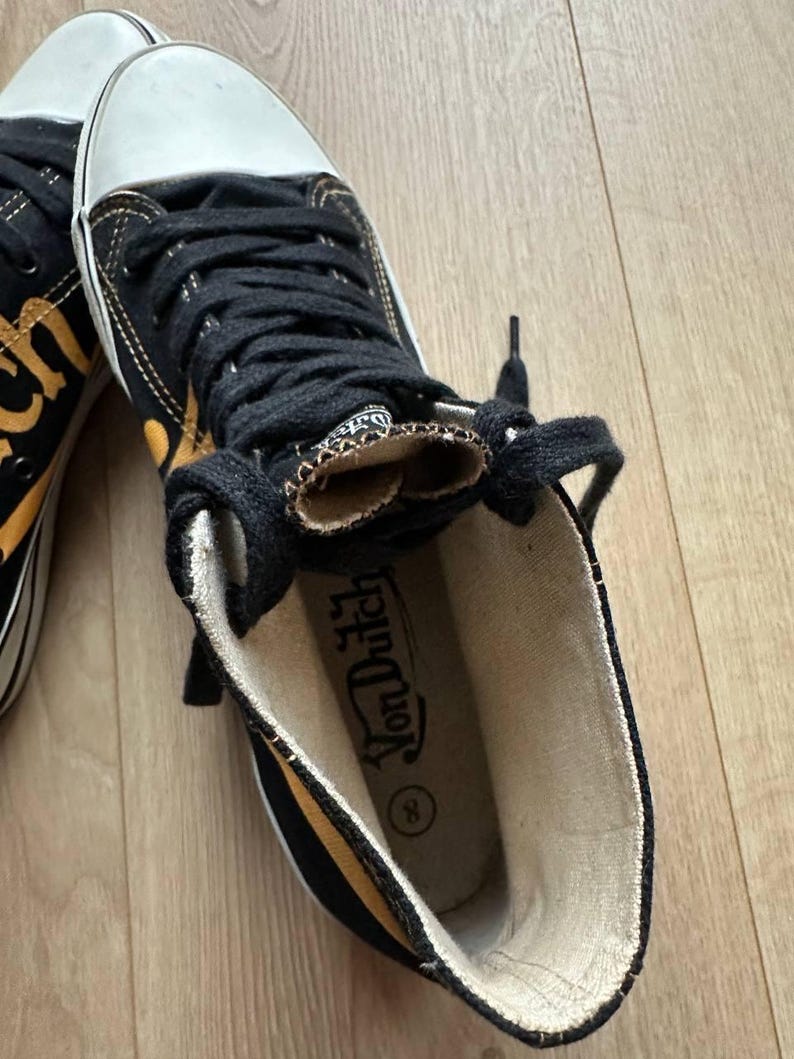 Puede incluir: Zapatillas altas negras y amarillas con punteras blancas y cordones negros. Las zapatillas tienen el logo "Von Dutch" en el interior. Los zapatos son de lona y tienen suela de goma.