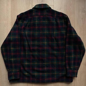 May include: A dark green, red, and yellow plaid flannel shirt. The shirt has a button-down collar and long sleeves with buttoned cuffs. The plaid pattern is a classic design, suitable for casual wear.
