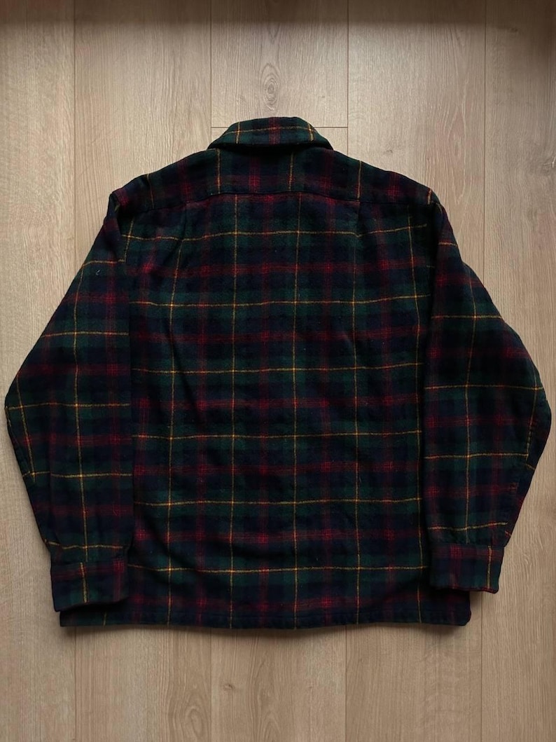 May include: A dark green, red, and yellow plaid flannel shirt. The shirt has a button-down collar and long sleeves with buttoned cuffs. The plaid pattern is a classic design, suitable for casual wear.