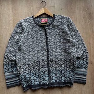 Pode incluir: Um cardigan cinza e azul estampado com gola redonda e fecho de botões. O design floral é complementado por punhos listrados. A etiqueta diz "HILVE".