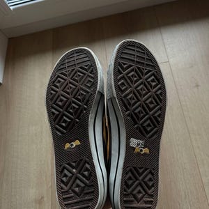 Puede incluir: Par de zapatillas marrones y blancas con suela texturizada. Las suelas tienen un patr&oacute;n geom&eacute;trico repetitivo y un logotipo de ojo alado. Los zapatos tienen una entresuela blanca y una raya negra.