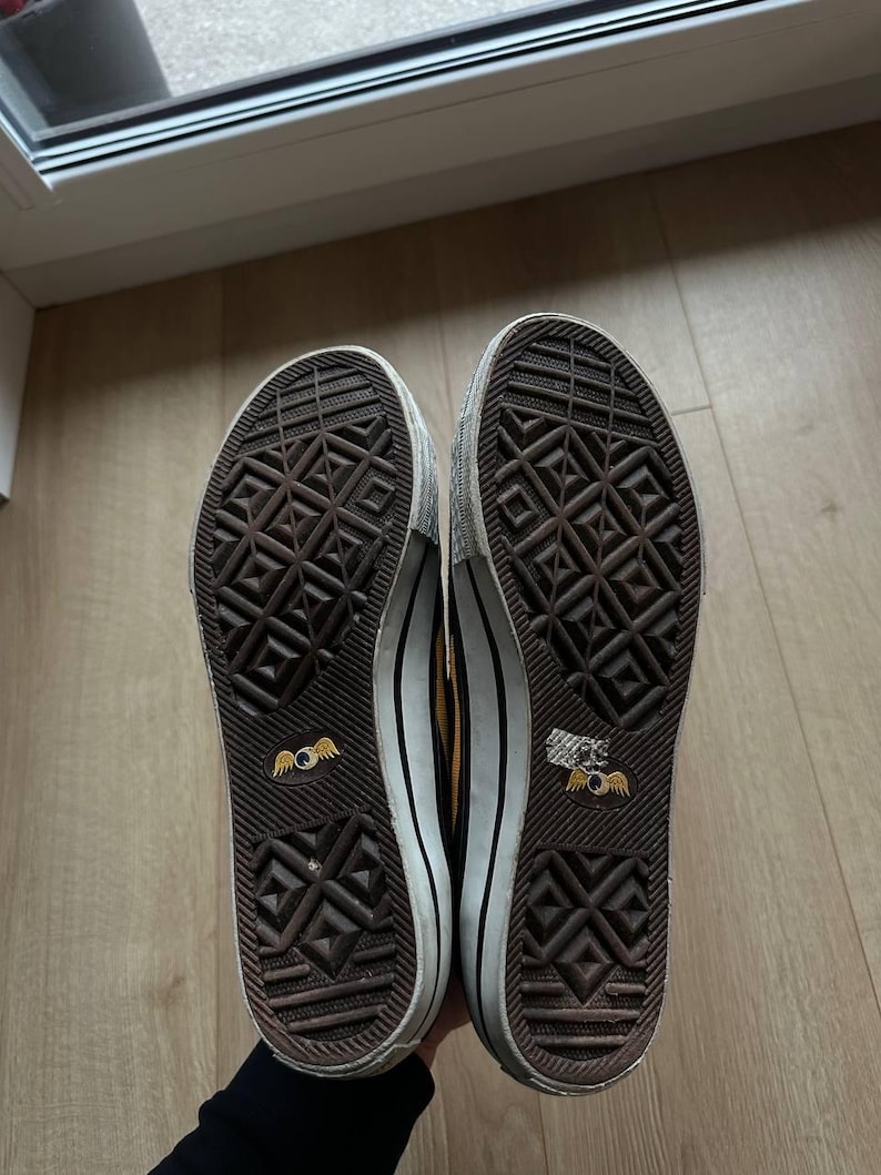 Puede incluir: Par de zapatillas marrones y blancas con suela texturizada. Las suelas tienen un patr&oacute;n geom&eacute;trico repetitivo y un logotipo de ojo alado. Los zapatos tienen una entresuela blanca y una raya negra.