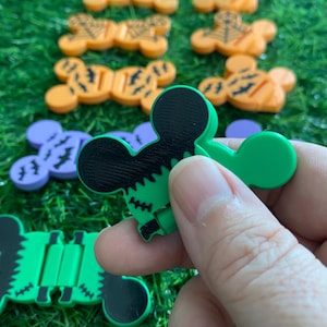 Peut inclure: Une collection d'organisateurs de câbles en plastique en forme de têtes de souris avec divers motifs sur le thème d'Halloween, notamment orange avec des toiles d'araignée, orange avec des chauves-souris, violet avec des chauves-souris et vert avec des coutures noires.