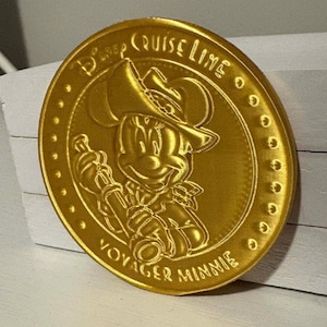 Puede incluir: Una moneda conmemorativa dorada con una imagen en relieve de Minnie Mouse con sombrero de vaquero. La moneda está inscrita con "Disney Cruise Line" y "Voyager Minnie". La moneda tiene una superficie detallada y texturizada y un fondo blanco.