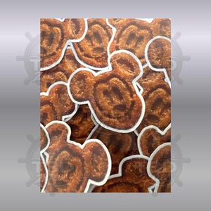 May include: A collection of die-cut stickers featuring a brown, textured, cartoon mouse head shape with rounded ears. Each sticker has a white border and depicts a golden-brown, crispy-looking food item with a smiling face and circular eyes.