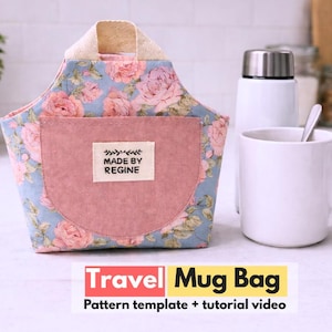 Könnte beinhalten: Eine Stofftasche für Becher mit blauem Hintergrund und rosa Rosenmuster, einer einfarbigen rosa Vordertasche und einem beigen Griff. Ein weißes rechteckiges Etikett auf der Tasche zeigt den Text MADE BY REGINE. Darunter steht Travel Mug Bag.