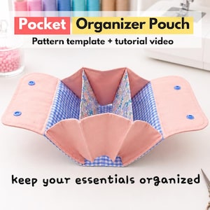 May include: A fabric pocket organizer pouch featuring a pink exterior, blue gingham interior, and floral patterned dividers. The pouch has two flaps with blue snap buttons. Text on the image reads: Pocket Organizer Pouch, Pattern template + tutorial video, keep your essentials organized.