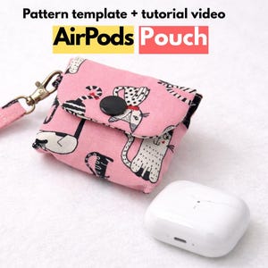 Może przedstawiać: Różowe etui na AirPods z paskiem na nadgarstek, z wzorem czarno-białych kotów. Etui ma czarne zapięcie na guzik i złote zapięcie. Tekst "AirPods Pouch" jest widoczny.