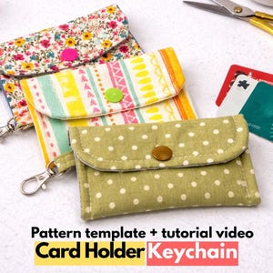 May include: Three fabric card holder keychains with metal lobster clasps. One features a floral print with a pink snap, one has a yellow and white striped pattern with a green snap, and one is olive green with white polka dots and a brown snap.