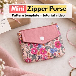 Könnte beinhalten: Eine Mini-Reißverschlusstasche mit Blumenmuster in Rosa, Blau und Weiß auf hellem Grund, ergänzt durch eine einfarbige rosa Klappe und einen weißen Druckknopf. Der Text "Mini Zipper Purse Pattern template + tutorial video" ist zu sehen.