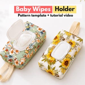 May include: Two rectangular fabric baby wipes holders with white plastic flip-top lids. One holder features a green background with a floral pattern, and the other has a white background with a sunflower print. Both include a beige fabric strap.