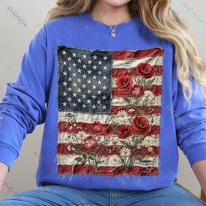 Könnte beinhalten: Blaues Langarm-Sweatshirt mit einem verblichenen Design der amerikanischen Flagge. Die Flagge zeigt rote und weiße Streifen, ein blaues Sternenfeld und florale Akzente aus roten Mohnblumen und weißen Gänseblümchen.