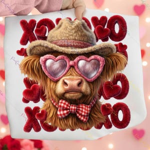 May include: A white tote bag featuring a Highland cow illustration. The cow wears heart-shaped sunglasses, a plaid bow tie, and a hat. Red, plush "XOXO" letters and hearts surround the cow, creating a Valentine's Day theme.