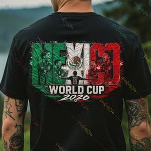 May include: A black t-shirt featuring a graphic print with the Mexican flag colors, images of soccer players, the text MEXICO, WORLD CUP, and 2026. The design includes a central player silhouette with the number 10 and a soccer ball graphic.