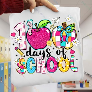 May include: White tote bag featuring a colorful design celebrating "100 days of school." The design includes a pink glitter apple, a worm, flowers, a pencil, and the words "days of school" in a playful font.