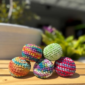 Puede incluir: Cinco peque&ntilde;as bolas esf&eacute;ricas tejidas a mano con hilo multicolor. Las bolas presentan varias combinaciones de colores, incluyendo un arco&iacute;ris brillante, verde claro s&oacute;lido y patrones jaspeados en naranja y azul, morado y blanco, y rojo y azul.