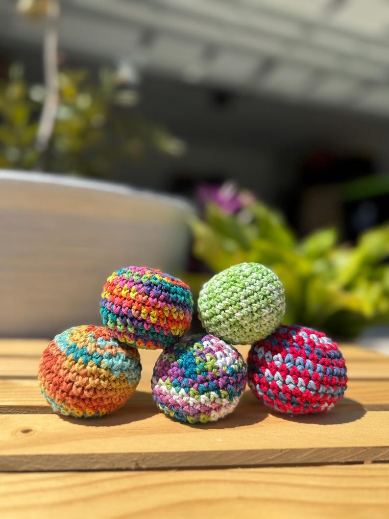 Puede incluir: Cinco peque&ntilde;as bolas esf&eacute;ricas tejidas a mano con hilo multicolor. Las bolas presentan varias combinaciones de colores, incluyendo un arco&iacute;ris brillante, verde claro s&oacute;lido y patrones jaspeados en naranja y azul, morado y blanco, y rojo y azul.