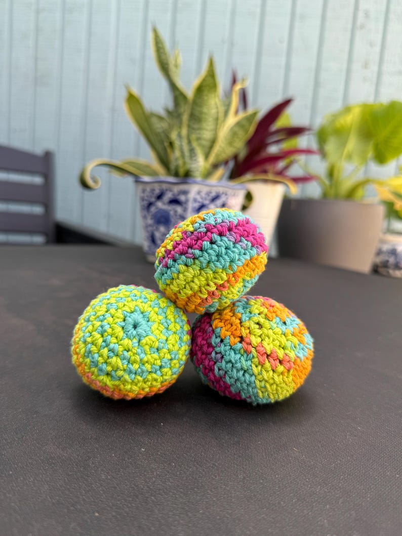 Puede incluir: Tres objetos esf&eacute;ricos elaborados con hilo multicolor mediante una t&eacute;cnica de ganchillo. El hilo presenta una mezcla vibrante de rosa brillante, verde lima, turquesa y naranja, creando un patr&oacute;n texturizado y variado en cada superficie.