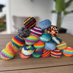 Puede incluir: Una colecci&oacute;n de peque&ntilde;as bolas redondas de ganchillo apiladas en forma de pir&aacute;mide. Las bolas presentan varios colores y patrones, incluyendo azul s&oacute;lido, rayas de arco&iacute;ris, texturas moteadas y combinaciones de hilos multicolores.