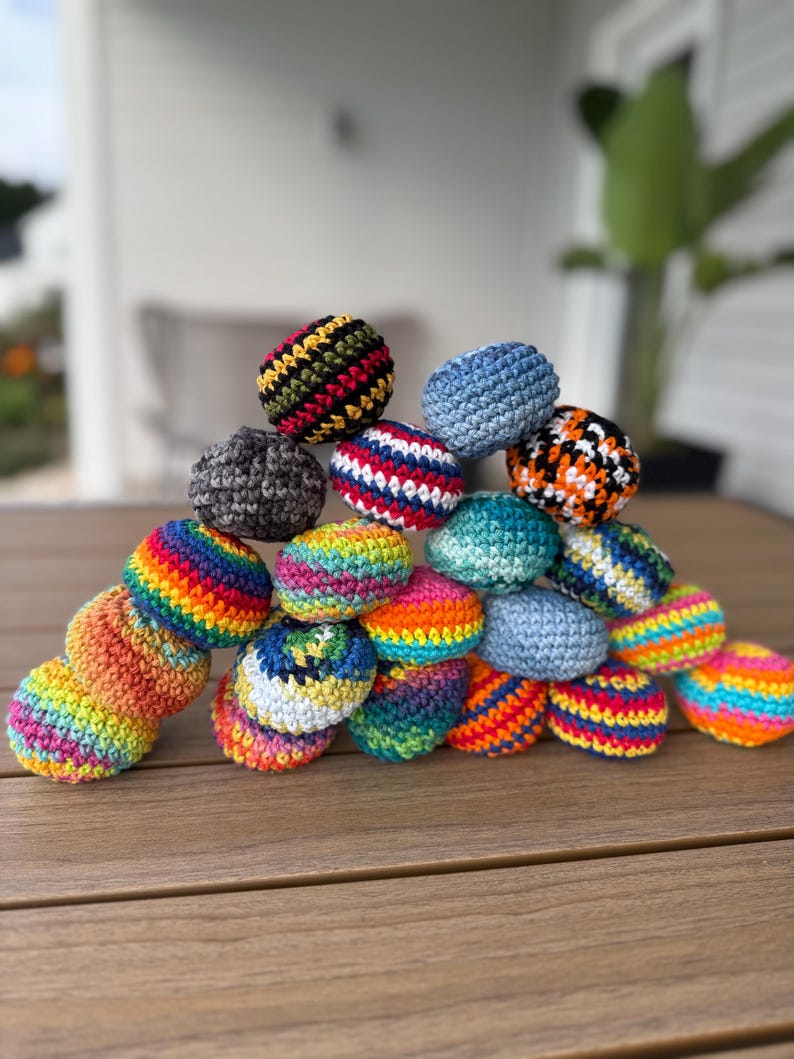 Puede incluir: Una colecci&oacute;n de peque&ntilde;as bolas redondas de ganchillo apiladas en forma de pir&aacute;mide. Las bolas presentan varios colores y patrones, incluyendo azul s&oacute;lido, rayas de arco&iacute;ris, texturas moteadas y combinaciones de hilos multicolores.