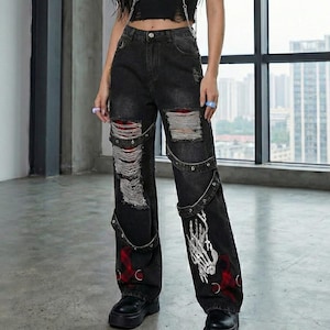 May include: Black distressed jeans with ripped knees and a skeleton hand design. The jeans are paired with a black crop top and a harness. The outfit is completed with black platform boots and a silver chain necklace.