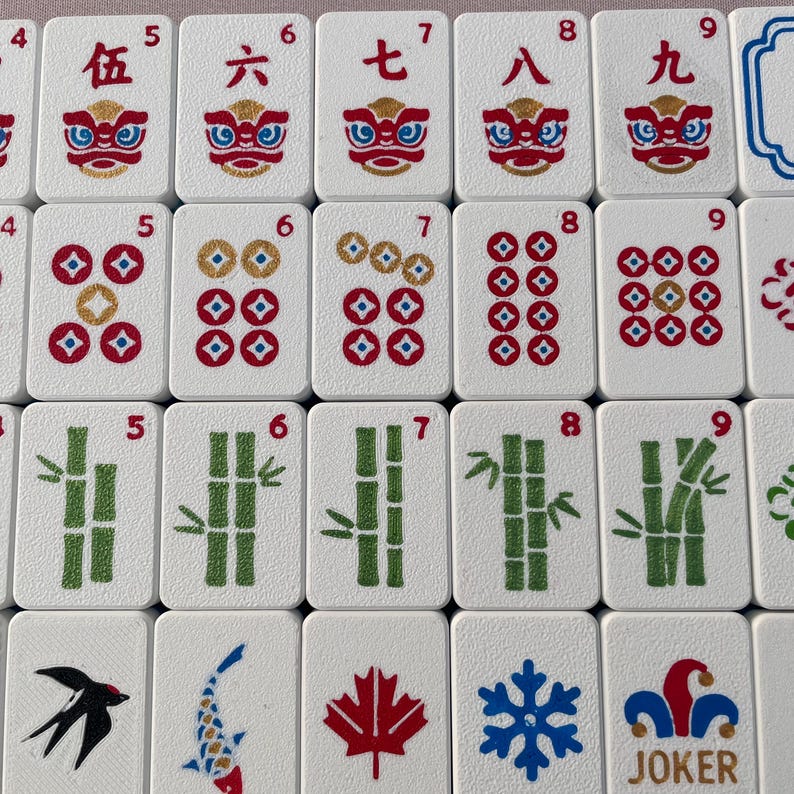 May include: A collection of white rectangular mahjong tiles featuring various designs including Chinese numerals, red lion faces, circular coin patterns, green bamboo stalks, a black bird, a koi fish, a red maple leaf, a blue snowflake, and a joker.