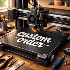 May include: A black 3D printer creating a white "custom order" design on a black surface. The printer has a fan, nozzle, and various mechanical components. Tools like pliers and a ruler are on the wooden surface.