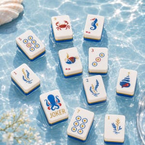 May include: A collection of white and blue Mahjong tiles with various illustrations, including a crab, seahorse, and octopus. The tiles are floating in water, creating a serene and playful scene. The word "JOKER" is printed on one tile.