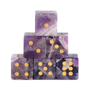 May include: Six amethyst dice stacked in a pyramid formation. Each die features gold-colored dots indicating the numbers. The dice are a mix of purple and white hues, with a polished finish.