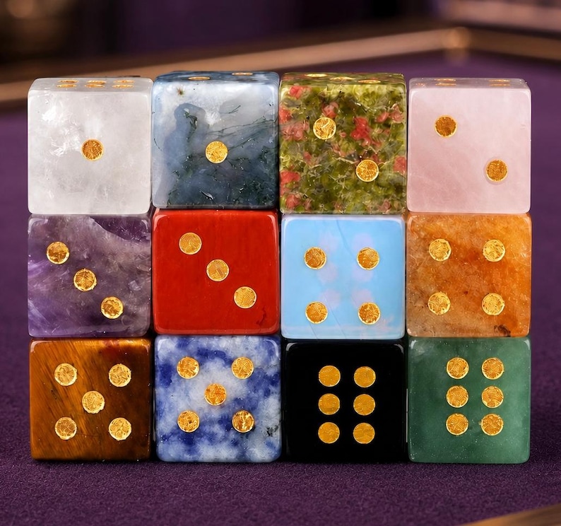 May include: A collection of twelve gemstone dice in various colors and patterns. Each die features gold-colored dots indicating the numbers. The dice are arranged in a grid, showcasing the diverse textures and hues of the gemstones, including amethyst, red jasper, and green jade.