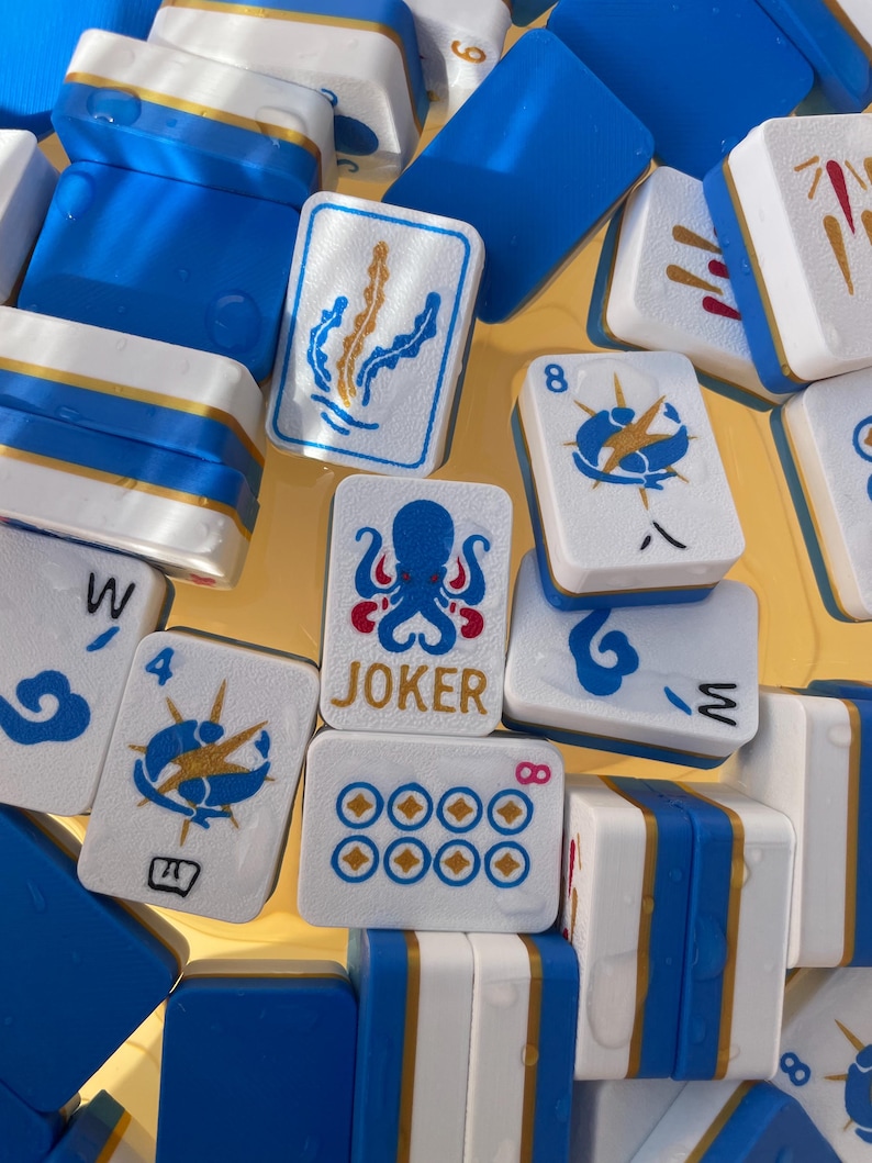 May include: A collection of blue, white, and gold Mahjong tiles. The tiles feature various symbols and numbers, including an octopus, seaweed, and the word "JOKER". The tiles are arranged closely together, creating a visually appealing pattern.