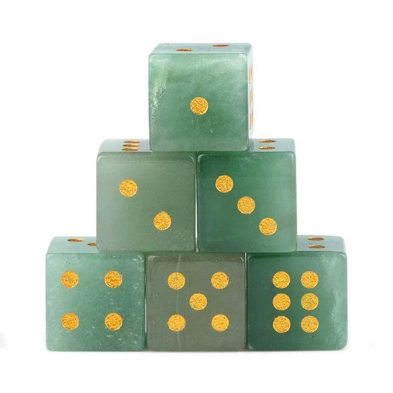 May include: Six green dice with gold-colored dots are stacked in a pyramid shape. The dice are made of a translucent material, and the dots are evenly spaced on each face. The dice are set against a white background.