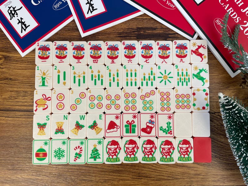 May include: A set of off-white mahjong tiles featuring festive holiday illustrations including Christmas trees, reindeer, Santa hats, stockings, gifts, and candles. The tiles are arranged in a grid on a wooden surface with game instruction cards.