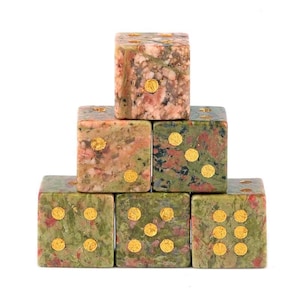 May include: A pyramid of six stone dice. The dice are a mix of green, pink, and brown with gold-colored dots. The dice are stacked on top of each other, with the top die showing one dot.