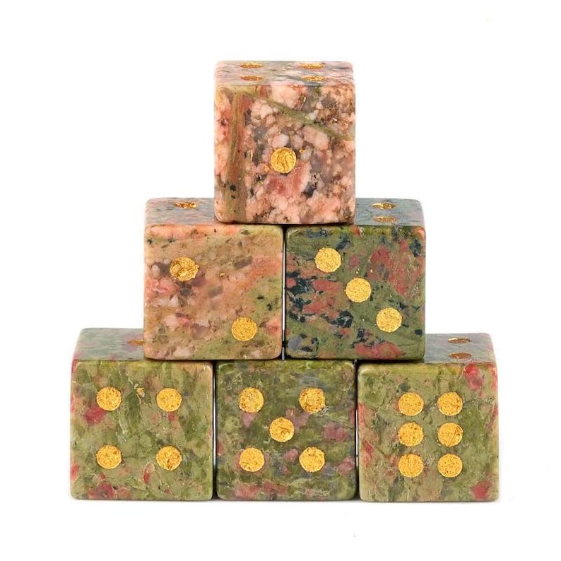 May include: A pyramid of six stone dice. The dice are a mix of green, pink, and brown with gold-colored dots. The dice are stacked on top of each other, with the top die showing one dot.