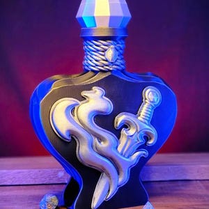 May include: A decorative bottle with a blue and black design, featuring a silver dragon and sword. The bottle has a geometric top and a rope-like neck. Dice are scattered around the bottle, suggesting a tabletop game theme.