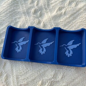 Puede incluir: Una bandeja azul de tres secciones con dise&ntilde;os de colibr&iacute;es. Cada secci&oacute;n presenta una silueta de colibr&iacute; azul claro. La bandeja est&aacute; hecha de un material s&oacute;lido y se encuentra sobre una superficie blanca texturizada.