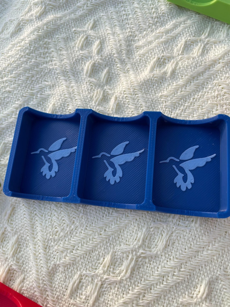 Puede incluir: Una bandeja azul de tres secciones con dise&ntilde;os de colibr&iacute;es. Cada secci&oacute;n presenta una silueta de colibr&iacute; azul claro. La bandeja est&aacute; hecha de un material s&oacute;lido y se encuentra sobre una superficie blanca texturizada.