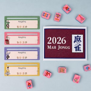 Könnte beinhalten: Eine Sammlung von Mahjong-Spielsteinen und Zubehör. Das Bild zeigt vier rechteckige Namensschilder in Grün, Rosa, Lila und Gelb, jeweils mit dem Wort "MAHJONG" und einer kleinen Illustration. Mehrere rosa Mahjong-Steine sind um eine Karte mit der Aufschrift "2026 MAH JONGG" verstreut.