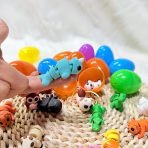 May include: A selection of brightly coloured plastic Easter eggs and miniature animal figures. A light blue segmented caterpillar is held by a finger. Other figures include a green alligator, a brown owl, and a black beetle.
