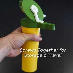 Puede incluir: Un dispositivo de plástico amarillo y verde con un asa y una parte superior circular. El texto "Screws Together for Storage & Travel" está impreso en el lateral. El dispositivo se sostiene en una mano.
